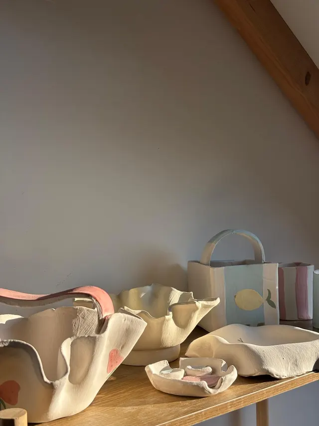 Hand-built ruffle bowls, a lemon basket and a striped cup on a sunlit wooden shelf